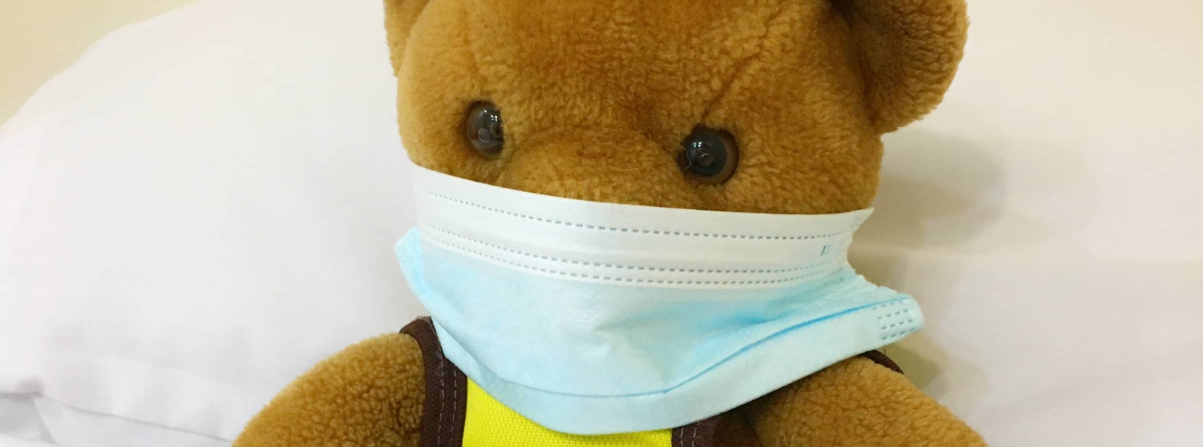 A child's teddy bear wearing a medical face mask